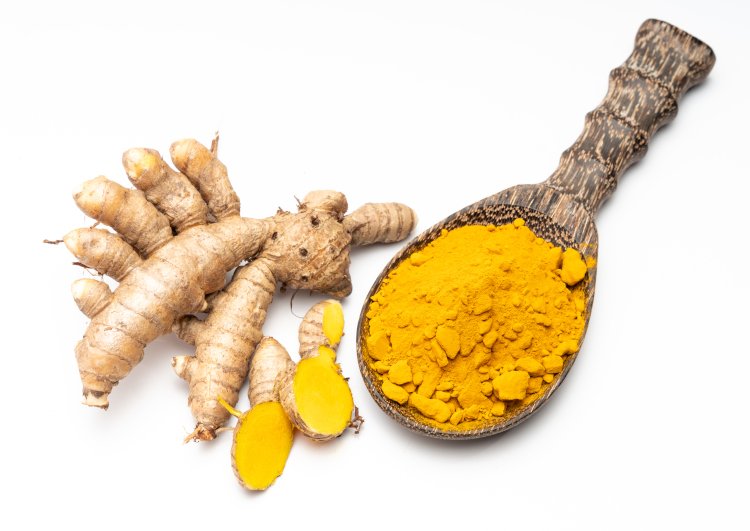 Fresh turmeric root and ground turmeric powder in a wooden spoon.